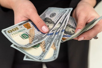 business lady in a black classic suit holds a bunch of new dollars in her beautiful hands.