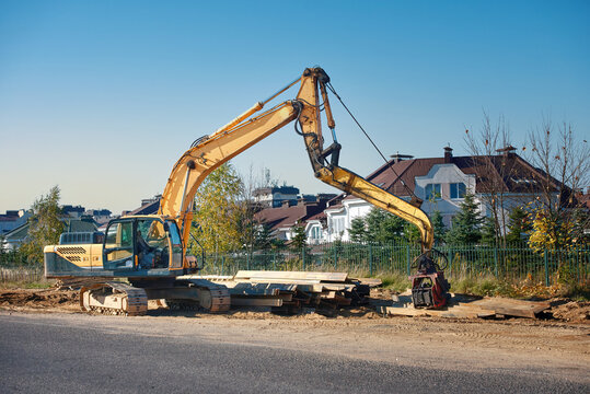 Excavator sheet pile driver, crawler mounted vibratory hammer. Crawler excavator hydraulic piling digger. Construction vehicle with vibro hammer. Rolled metal H-beam lay on the ground