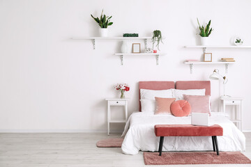 Comfortable bed, nightstands, vase with flowers and houseplants near white wall