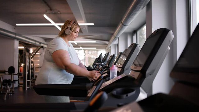 Overweight woman with headphones exercising on treadmill in gym