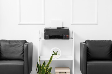 Comfortable armchairs and shelf unit with modern printer near light wall