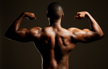 The bigger the muscle the better the man. Rearview studio shot of a fit young man flexing against a black background.