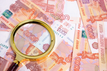 Magnifying magnifier against background Russian rubles with face value five thousand.