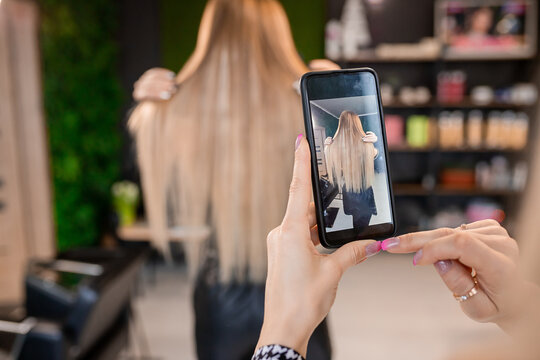 Professional hairdresser taking photo of blonde client's hair extensions for social media showcase - Powered by Adobe