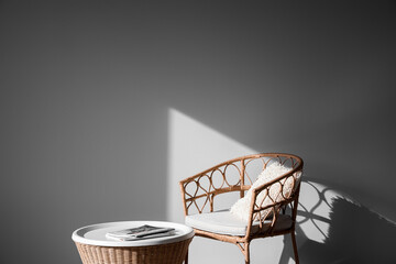 Rattan table with magazines and wicker armchair near grey wall