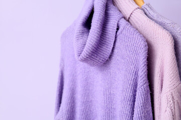 Lilac sweaters hanging on color background, closeup