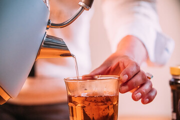 Female pouring tea from a tea pot into a glass. Close-up. High quality photo