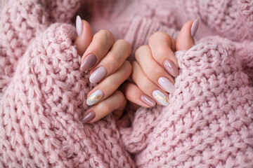 Women's hands with a beautiful  oval manicure in a warm pink knitted sweater. Winter trend, polish...