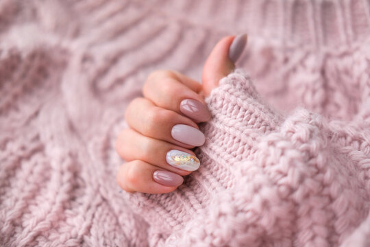 Women's hands with a beautiful  oval manicure in a warm pink knitted sweater. Winter trend, polish beige nails with gel polish, shellac. Copy space.