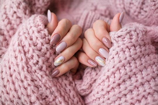 Women's hands with a beautiful  oval manicure in a warm pink knitted sweater. Winter trend, polish beige nails with gel polish, shellac. Copy space.
