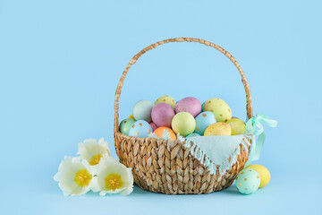 Wicker basket of painted Easter eggs and flowers on blue background