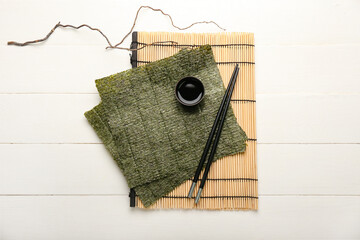 Bamboo mat with tasty seaweed sheets, chopsticks and bowl of soy sauce on light wooden background © Pixel-Shot