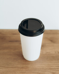 Cup of coffee to go in white paper cup on wood table. Morning