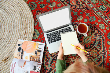 Woman with notebook and laptop on vintage carpet at home