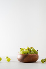 Ripe green gooseberries in a wooden bowl on a white background. Harvest concept. Vegetarian food. Side view, copy space. Gardening