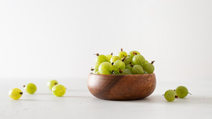 Ripe green gooseberries in a wooden bowl on a white background. Harvest concept. Vegetarian food. Side view, copy space. Gardening