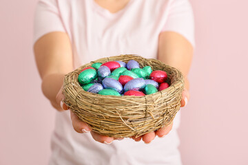 Fototapeta na wymiar Woman holding nest with chocolate eggs on color background, closeup