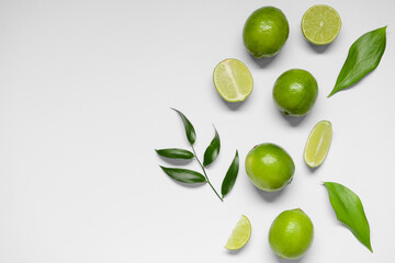 Fresh juicy limes and leaves on light background
