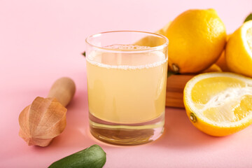 Glass of lemon juice and wooden juicer on pink background, closeup