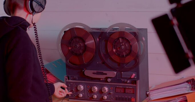 Child starts the retro reel to reel tape recorder with spinning reels, uses headphones. Popular disco trends 60s, 70s, 80s. 