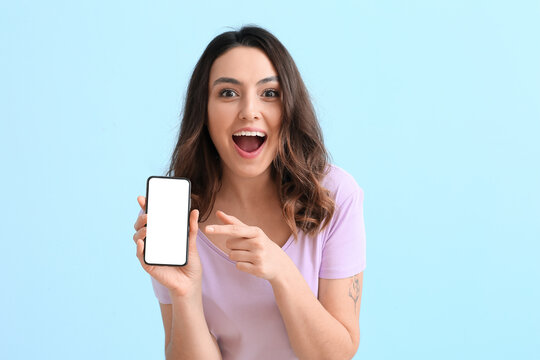 Excited young woman with mobile phone on blue background