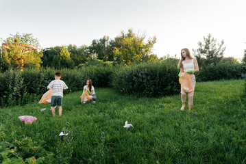 A group of adults and children together at sunset is engaged in garbage collection in the park....