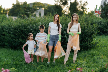 Fototapeta premium A group of adults and children together at sunset is engaged in garbage collection in the park. Environmental care, waste recycling. Sorting garbage.