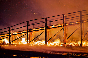 Burning wooden bridge in a raging flame close-up. Bridge on fire at dark night. Transition in Bright Hellfire. Hellfire Bridge. Bridge during intense combustion and heating. Wooden structures on fire.