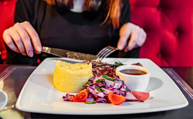 woman hands with fork and knife eating beef steak wiht salad in cafe