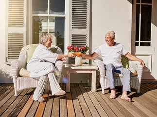 Heres to more mornings like this. Shot of a happy senior couple toasting with juice on the patio at home.