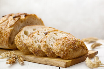 Close up of sliced traditional round wheat bread on linen towel with ears of wheat around, selective focus.