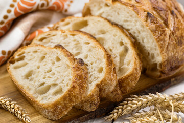 Sliced freshly homemade wheat bread on wooden board on light background, selective focus.
