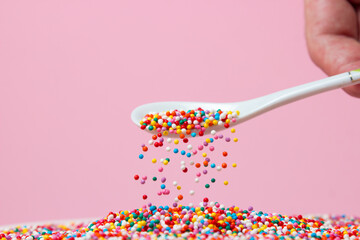 Confectionery sprinkles are sprinkled from a spoon on a pink background. Topping for desserts and...