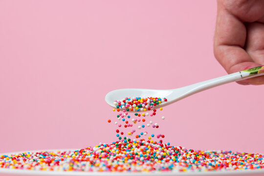 Confectionery sprinkles are sprinkled from a spoon on a pink background. Topping for desserts and pastries. small caramel balls