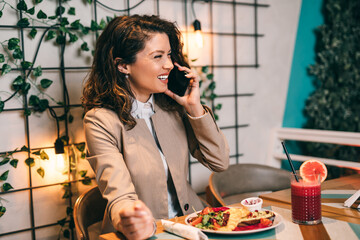 A beautiful middle-aged woman is sitting in a restaurant, talking on the mobile phone and enjoys a healthy and fresh beetroot and grapefruit juice..