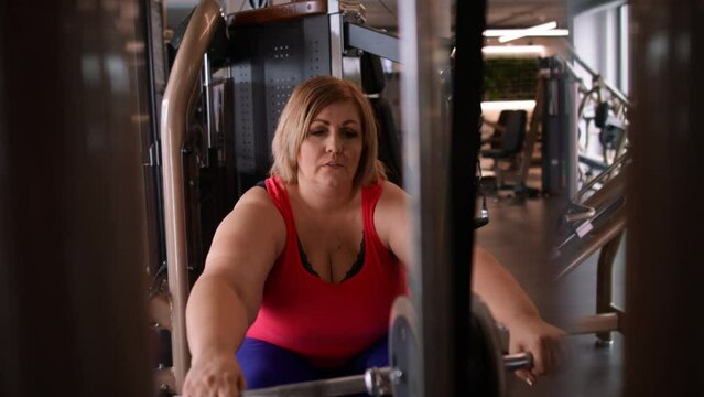 Fat woman working out on a lat pulldown machine indoors in gym