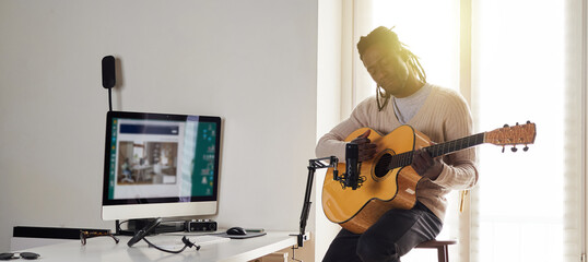 Young man is singing and playing guitar while making an audio recording at home