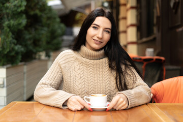 Portrait of a smiling woman in a street cafe with a cup of coffee, businesswoman lifestyle, morning breakfast outdoors, urban lifestyle