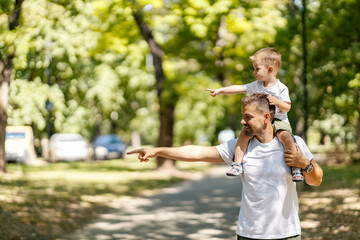 Father and son having piggyback ride and both pointing at something in the forest.