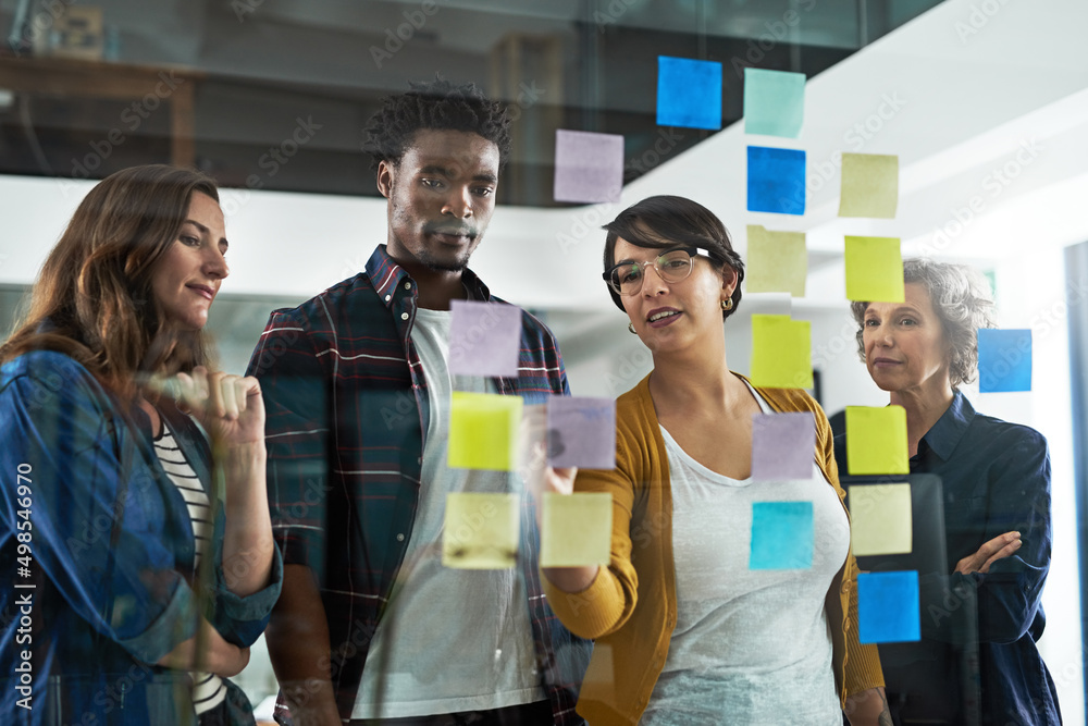 Poster multiplying their success by dividing their tasks. shot of a group of colleagues working with adhesi