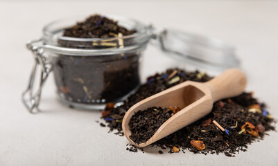 Black tea in a wooden spoon and glass jar. Composition on a light textural background. side view. Place for text.