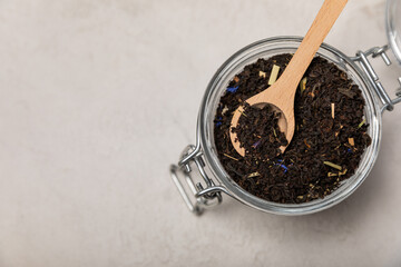 Black tea in a wooden spoon on the background of a glass jar. Composition on a light textural...