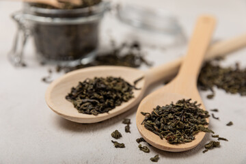 Leaves of green fragrant tea in wooden spoons on a gray textural background. Side view. Place for text