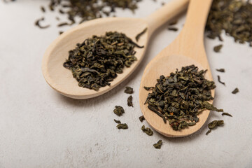 Leaves of green fragrant tea in wooden spoons on a gray textural background. Side view. Place for text
