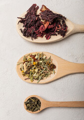 Various types of tea in wooden spoons on a light texture background. Tea mixture. Range. Black, green, herbal and hibiscus teas. Top view. Copy space.Various types of tea in wooden spoons on a light t