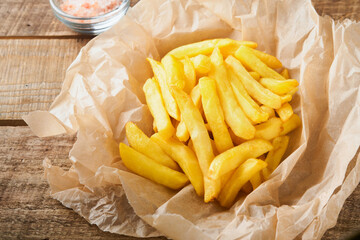 French fries. Tasty French fries server on parchment paper on wooden cutting board with tomato and cheese sauce on wooden table background. Diverse Keto Dishes. Fast food and unhealthy food concept.