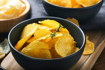 Potato corrugatedchips. Fast food. Crispy potato chips ceramic black bowl with sour cream sauce and onions in wooden stand on old kitchen table wooden background. American tradition. Hot BBQ. Top view