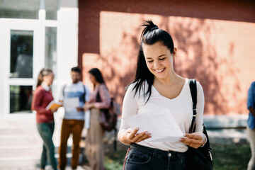 Young happy woman reading her test results in front of university building.
