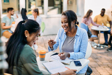Happy African American woman and her college friend talk while studying on coffee break at campus.