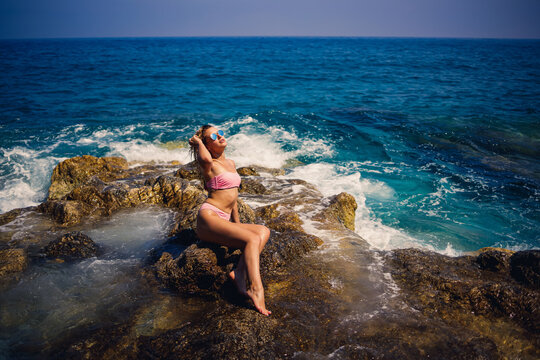 Young beautiful woman in a swimsuit sits on a rocky beach of the Mediterranean sea in Turkey. The concept of sea recreation. Selective focus